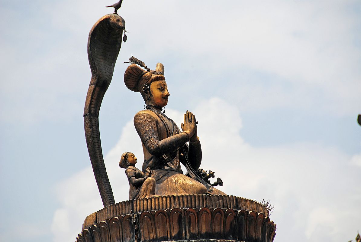 Kathmandu Patan Durbar Square 11 King Yoganarendra Malla Column Close Up The King Yoganarendra Malla column (1700) in Patan�s Durbar Square is topped by a golden statue of a kneeling King Yoganarendra Malla and his queens on a lotus, protected by the hood of a cobra with a bird on his head.